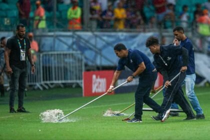 Funcionários passam rodos no gramado da Arena Fonte Nova para diminuir o impacto das chuvas